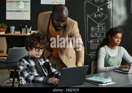 African American teacher teaching children to work with computer at table during IT lesson in classroom Stock Photo