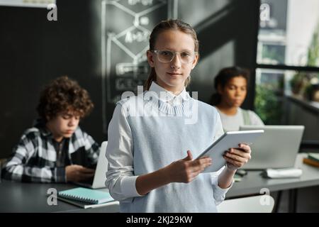 Portrait of schoolgirl in eyeglasses looking at camera using digital tablet during IT lesson Stock Photo