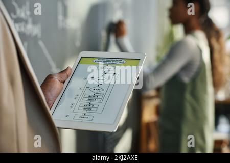 Close-up of teacher using digital tablet with graphs on screen with child writing on blackboard in background Stock Photo
