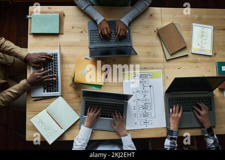 High angle view of teacher sitting at wooden table together with children at IT lesson, they typing on laptop computers to develop new software in tea Stock Photo