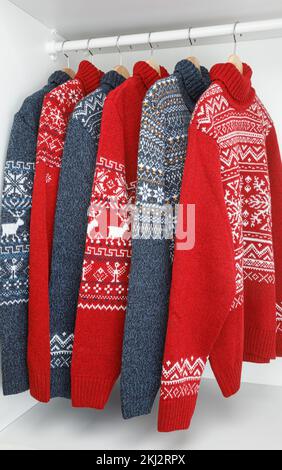 Various knitted Christmas turtleneck pullovers with nordic geometric ornament (aka Ugly sweaters) on hanger rack in a store Stock Photo