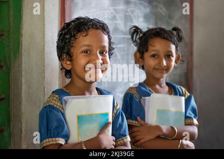 Three School Children's holding books standing at school Stock Photo