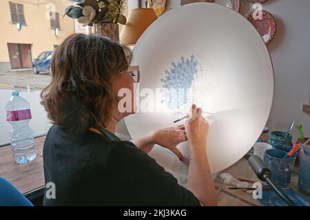 Decorator painting a ceramic plate in her workshop, Deruta village, Perugia, Umbria, Italy Stock Photo