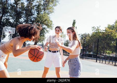 Multicultural group of young female friends bonding outdoors and having fun. Stylish cool teen girls gathering at basketball court, friends playing ba Stock Photo