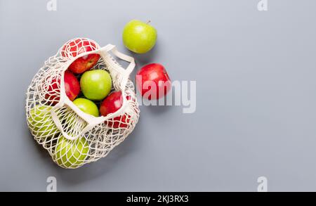 Red and green apples in mesh bag on grey background. Flat lay with copy space Stock Photo