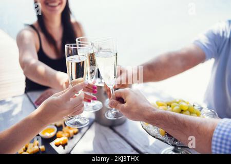 Happy people on the beach having a party, drinking and having a lot of fun in the sunset, they are wearing smart casual clothes and drink champagne Stock Photo