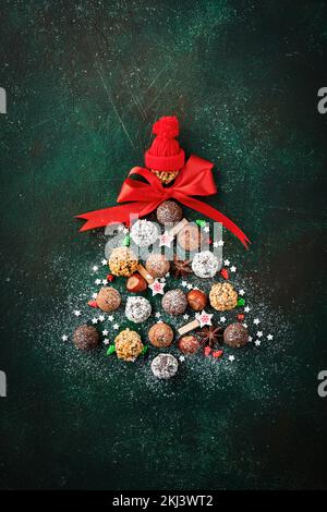 Christmas tree made of chocolate truffles, hazelnuts, anise stars, decorations, spoons and powdered sugar snow on dark green background. Christmas hol Stock Photo