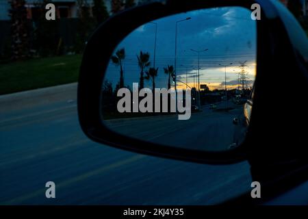 Palm trees and the beautiful bright red sunrise or sunset of the city are reflected in the car's side mirror. Stock Photo
