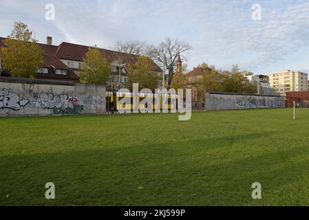 A tram passes along Bernauer Strasse behind a remaining part of the Belrin Wall, at the Berlin Wall memorial site, Berlin, Germany Stock Photo