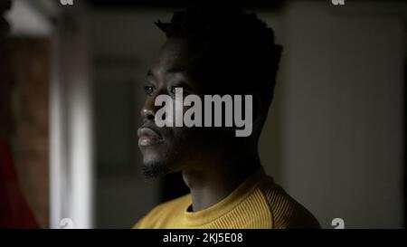 African man standing by window thinking about life. Concerned worried emotion Stock Photo