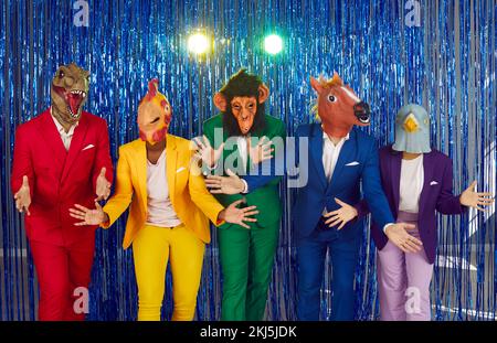 People in funny masks of heads of different animals are dancing at disco party on shiny background. Stock Photo