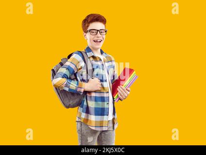 Happy, handsome red-haired boy in transparent glasses, holding backpack and textbooks. Stock Photo