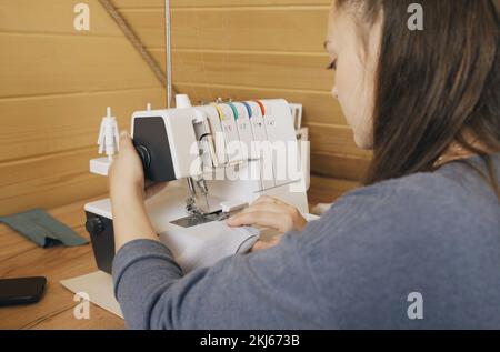 A woman designer works on an overlock sewing machine on tailoring. Small tailoring business. Stock Photo