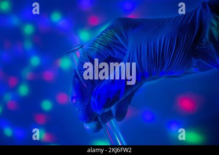 Laboratory test tube in the hand of a doctor in a blue glove against the background of multi-colored bokeh in the evening. Test immunization and Stock Photo