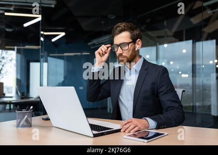Mature serious thinking businessman working inside office, boss investor in business suit working at table with laptop brainstorming business strategy and plan. Stock Photo