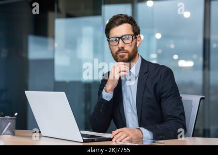 Mature serious thinking businessman working inside office, boss investor in business suit working at table with laptop brainstorming business strategy and plan. Stock Photo