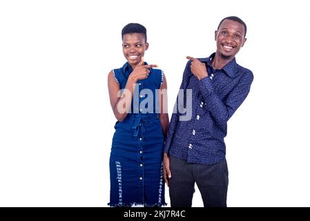 portrait of a young man and woman pointing the index fingers towards each other while smiling at the camera. Stock Photo