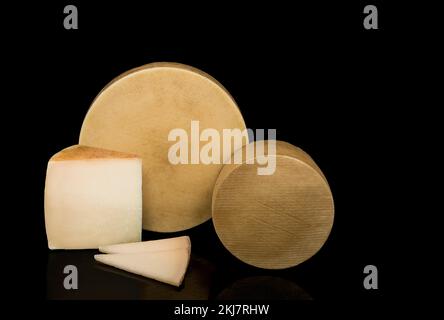 Two cheeses one large and one small isolated on a black background with texture in their rinds next to a wedge and pieces of cheese. Stock Photo