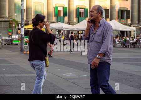 Two people walking in opposite directions at Dante's Square in Naples. In the background there are children playing Stock Photo