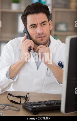 male doctor using telephone while working on computer in clinic Stock Photo