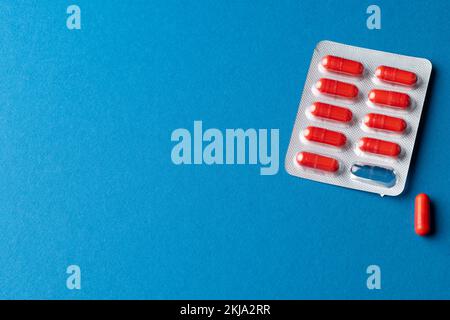 Composition of red pills in blister pack, and one pill out, on blue background with copy space Stock Photo