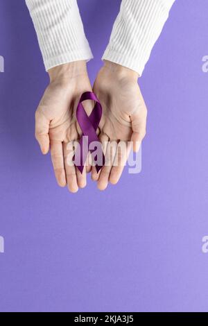 Vertical of hands holding purple cancer awareness ribbon on purple background with copy space Stock Photo