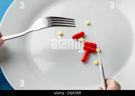 Composition of hands holding fork and knife over plate with various pills Stock Photo
