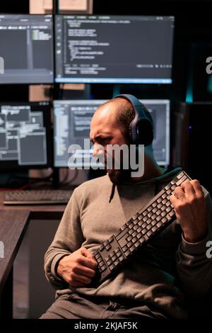 Funky developer singing at air guitar keyboard late at night, working on cloud computing html script. Having fun with artificial intelligence and data on terminal window, fooling around. Stock Photo