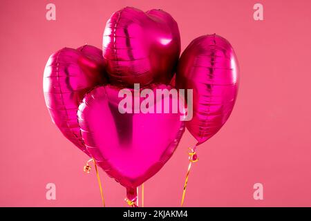 Four shiny pink heart shaped balloons floating on pink background with ...