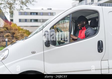 Black young adult delivery guy sitting inside white van working on laptop computer. Delivery service. Horizontal outdoor shot. High quality photo Stock Photo