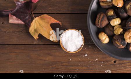 Roasted chestnuts in cast iron pan over rustic wooden board and grey wooden background, selective focus. Stock Photo