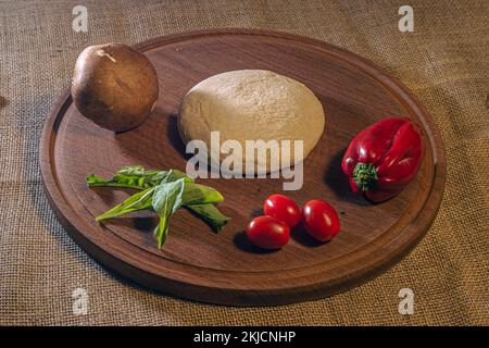 Preparation italian pizza dough with vegetables on table.  Stock Photo