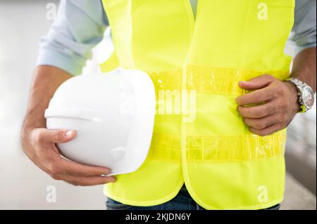 Engineer is holding hardhat wearing a yellow vest and standing ready for work safety on site. Stock Photo
