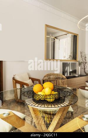 Round glass table and wooden legs with decorative black wire centerpiece filled with ripe citrus in a contemporary decorated living room Stock Photo