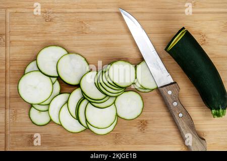 raw zucchini with a sharp knife and stack many thin slices on a bamboo board viewed in top view Stock Photo