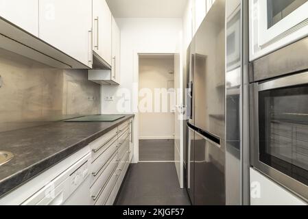 kitchen with white lacquered cabinets, gray wood countertops and built-in stainless steel appliances Stock Photo