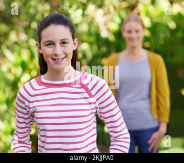 Shes growing up to be a wonderful woman. a teenage girl standing outdoors with her mother in the background. Stock Photo