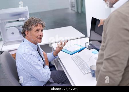 The thing is...A mature businessman sitting at his workstation explaining something to his colleague. Stock Photo