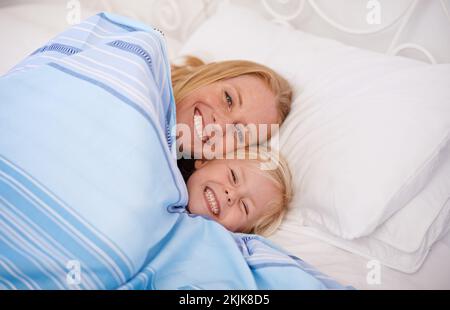 Snuggling together under the covers. a mother and her young daughter lying in bed together. Stock Photo