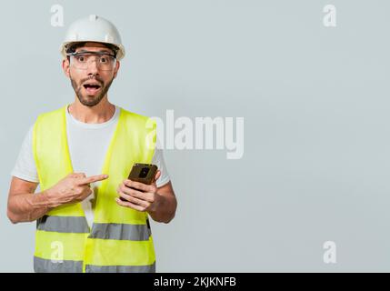 Engineer using and pointing at cellphone. Amazed construction worker using and pointing cellphone. Surprised face engineer using cell phone. Construct Stock Photo