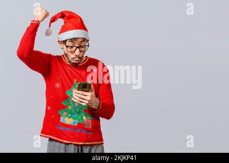 People in santa hat looking at cell phone excited, Excited young man in christmas hat using cellphone celebrating, Excited guy in christmas hat lookin Stock Photo