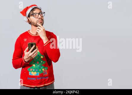 Handsome man in christmas clothes thoughtful holding cell phone. Thoughtful man with christmas hat holding cell phone, Young man in christmas clothes Stock Photo