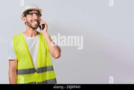 Young builder engineer in vest talking on cell phone isolated. Civil engineer concept talking on cellphone isolated, Smiling engineer talking on the p Stock Photo