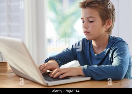 Zipping through his homework. a young boy using a laptop at home. Stock Photo