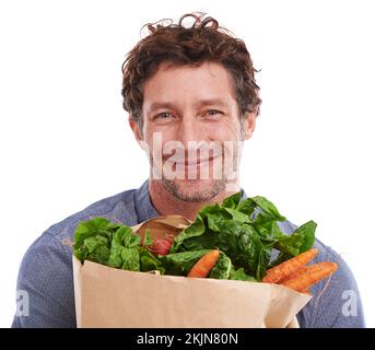 Bringing home the veggies. Studio portrait of a handsome young man holding a shopping bag full of fresh vegetables. Stock Photo