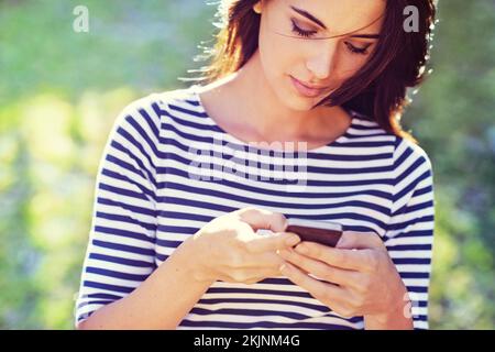Sharing her day with a special someone. a gorgeous young woman using her mobile phone while outside. Stock Photo
