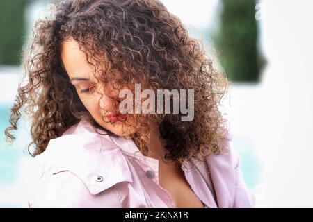 A beautiful Hispanic woman with painted lips and curly hair looking down Stock Photo