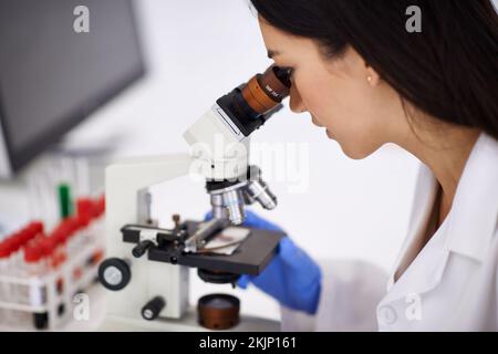 Keeping safe which working with blood. Profile of a female scientist viewing a sample through a microscope. Stock Photo
