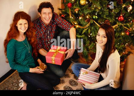 Jolly friends by the xmas tree. Portrait of a group of young friends sitting by a Christmas tree with their presents. Stock Photo