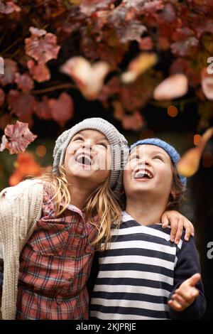 Autumn joy. Two cute kids lauging joyfully while watching Autumn leaves falling from the trees. Stock Photo